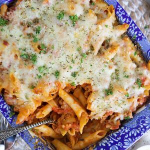 A serving spoon is placed in a dish filled with baked mostaccioli.