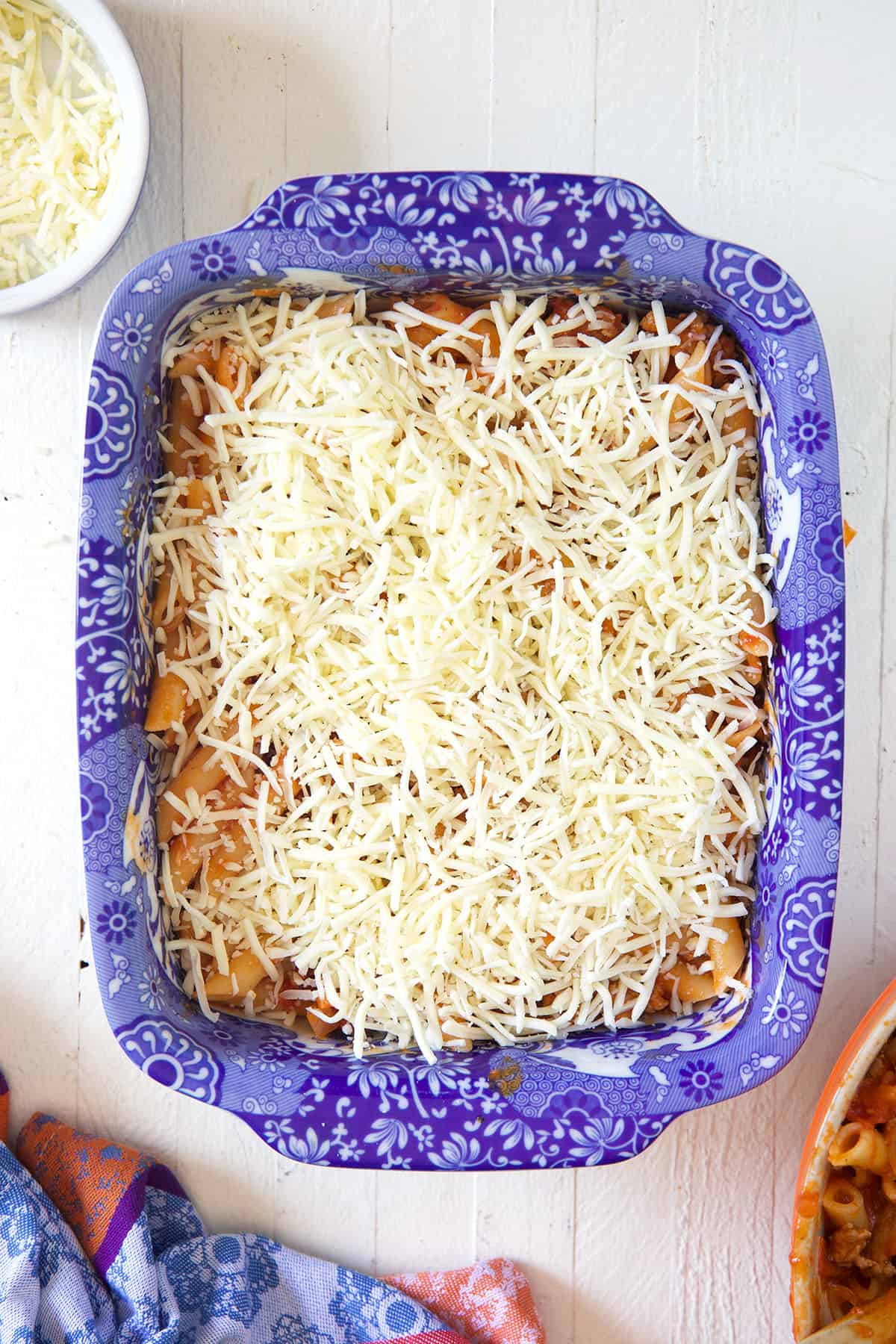 Shredded cheese is sprinkled evenly on top of saucy pasta in a baking dish.