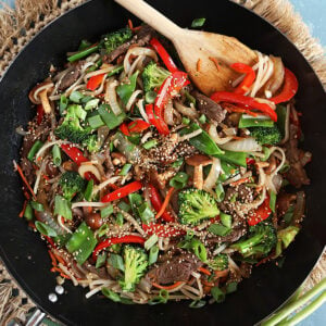 Overhead shot of beef stir fry in a black wok with a wooden spoon.