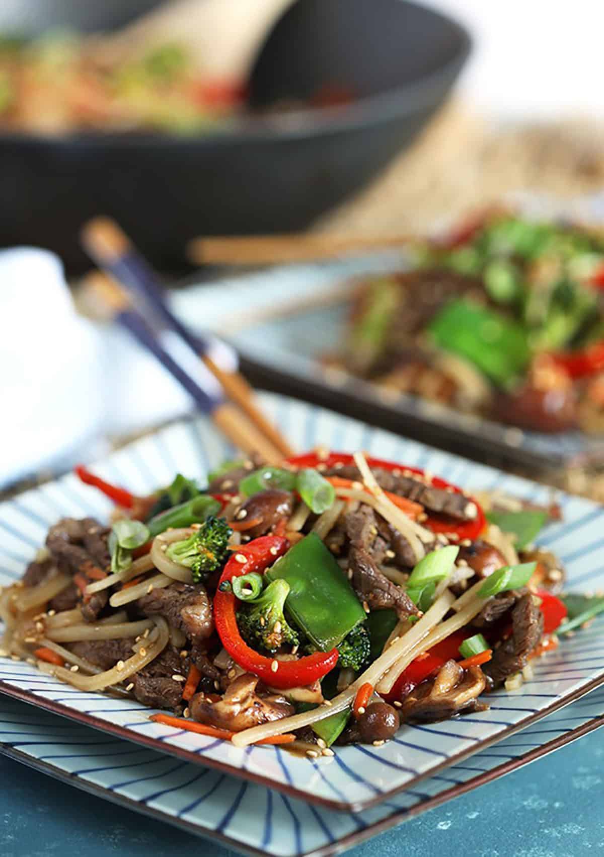 Beef Stir Fry with noodles on a square plate with wood chopsticks. 