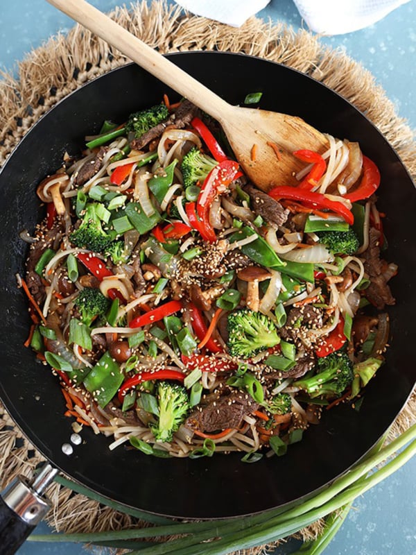 Overhead shot of beef stir fry in a black wok with a wooden spoon.