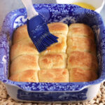 Dinner rolls in a baking dish after baking with a blue brush basting with butter.