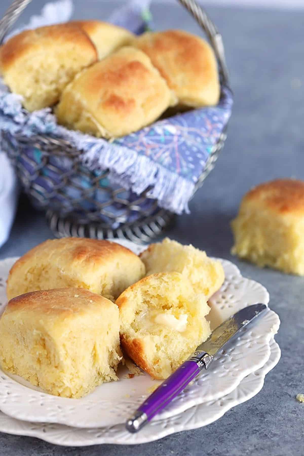 Dinner rolls in a basket with a dinner roll on a white plate.
