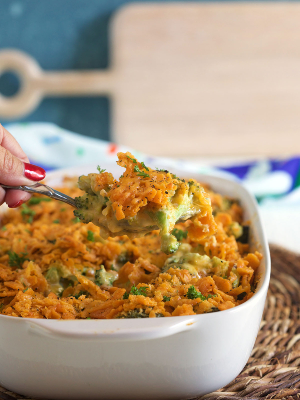 A small serving of casserole is being lifted from a white baking dish.
