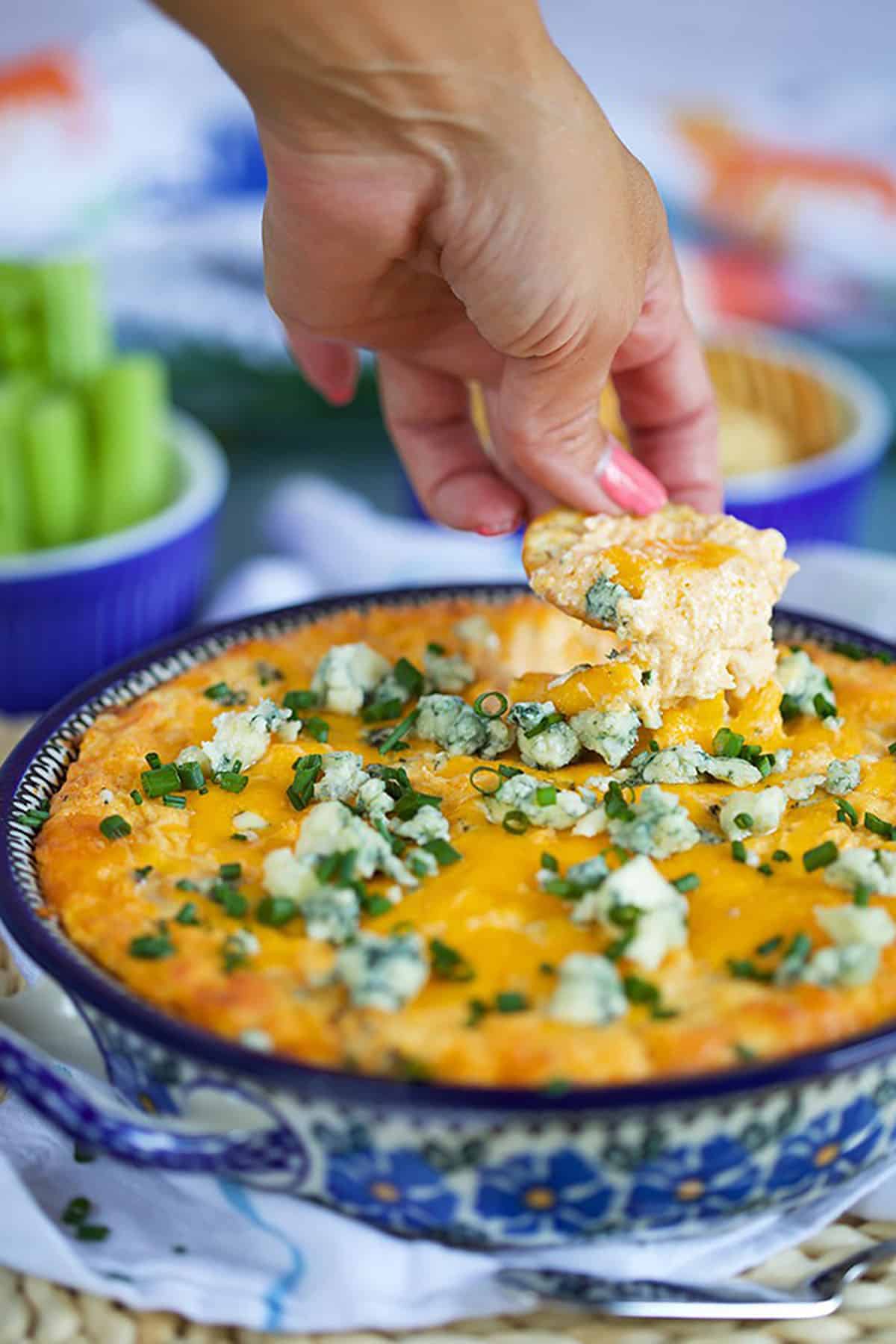 Buffalo Chicken Dip in a floral baking dish with a hand dipping a chip into the dip 