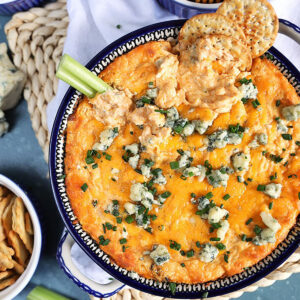 Overhead shot of buffalo chicken dip with blue cheese and crackers on top on a blue background.