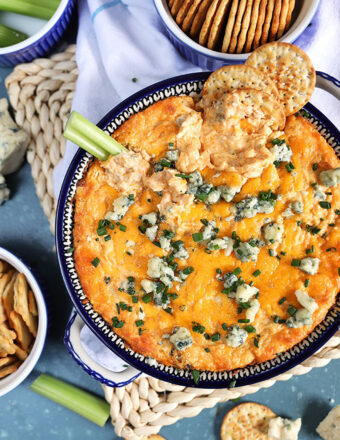 Overhead shot of buffalo chicken dip with blue cheese and crackers on top on a blue background.
