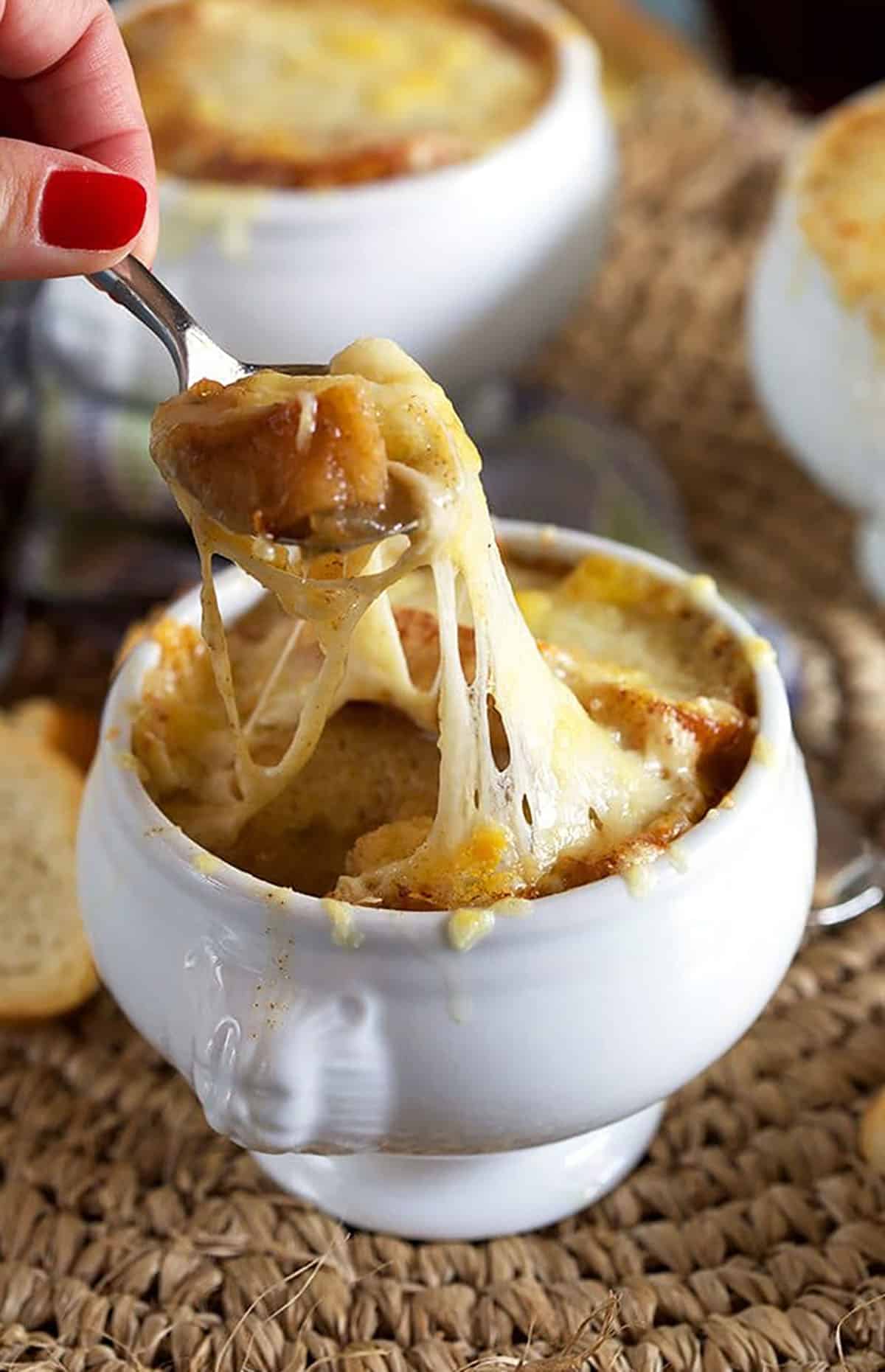 French onion soup in a white crock with a spoon cheese pull.