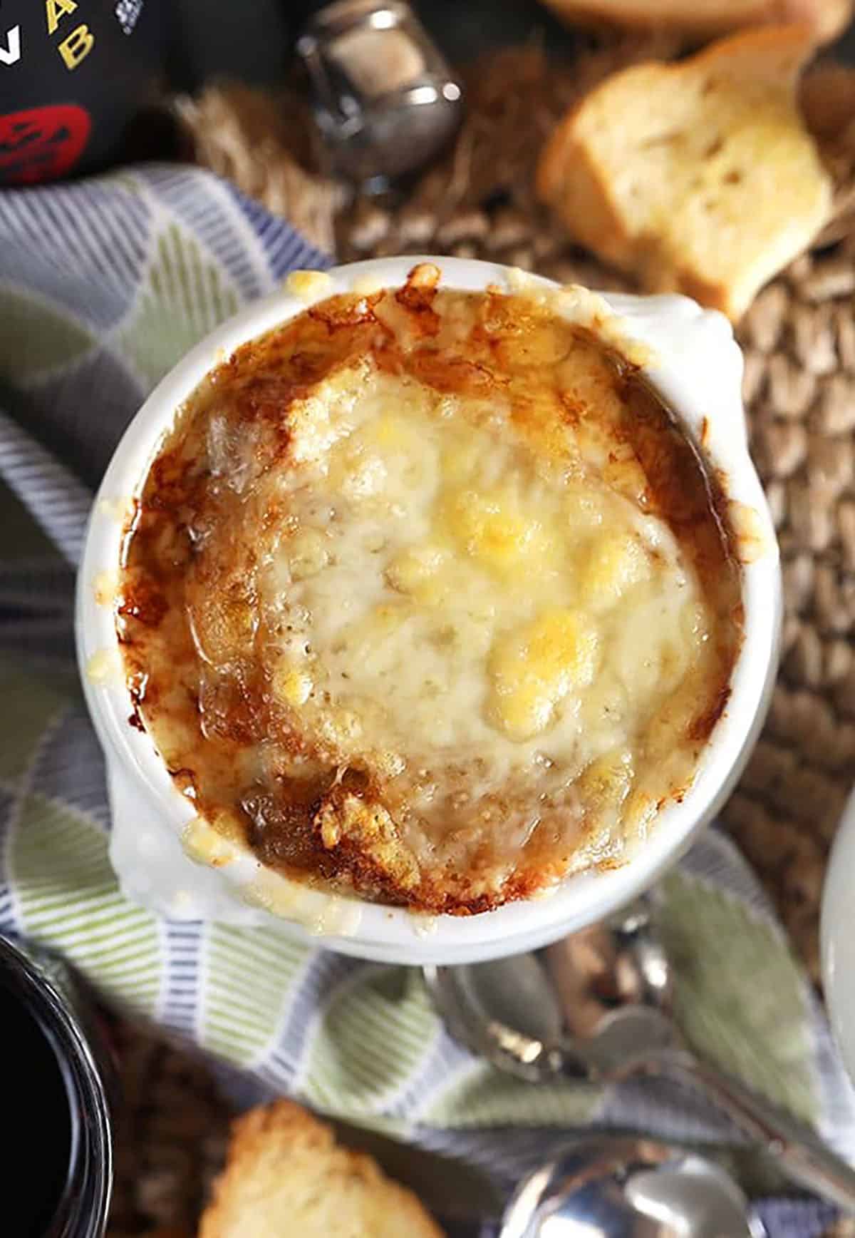 Melted, golden cheese on top of French onion soup in a white crock.