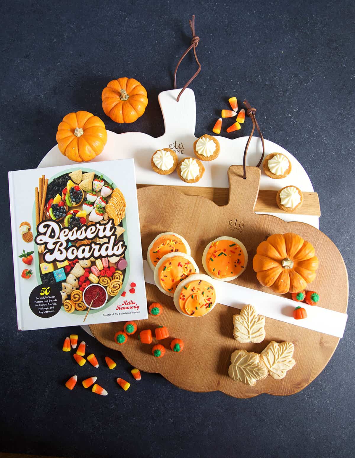 A dessert board cook book is positioned on pumpkin serving platters next to mini pumpkins and cookies.