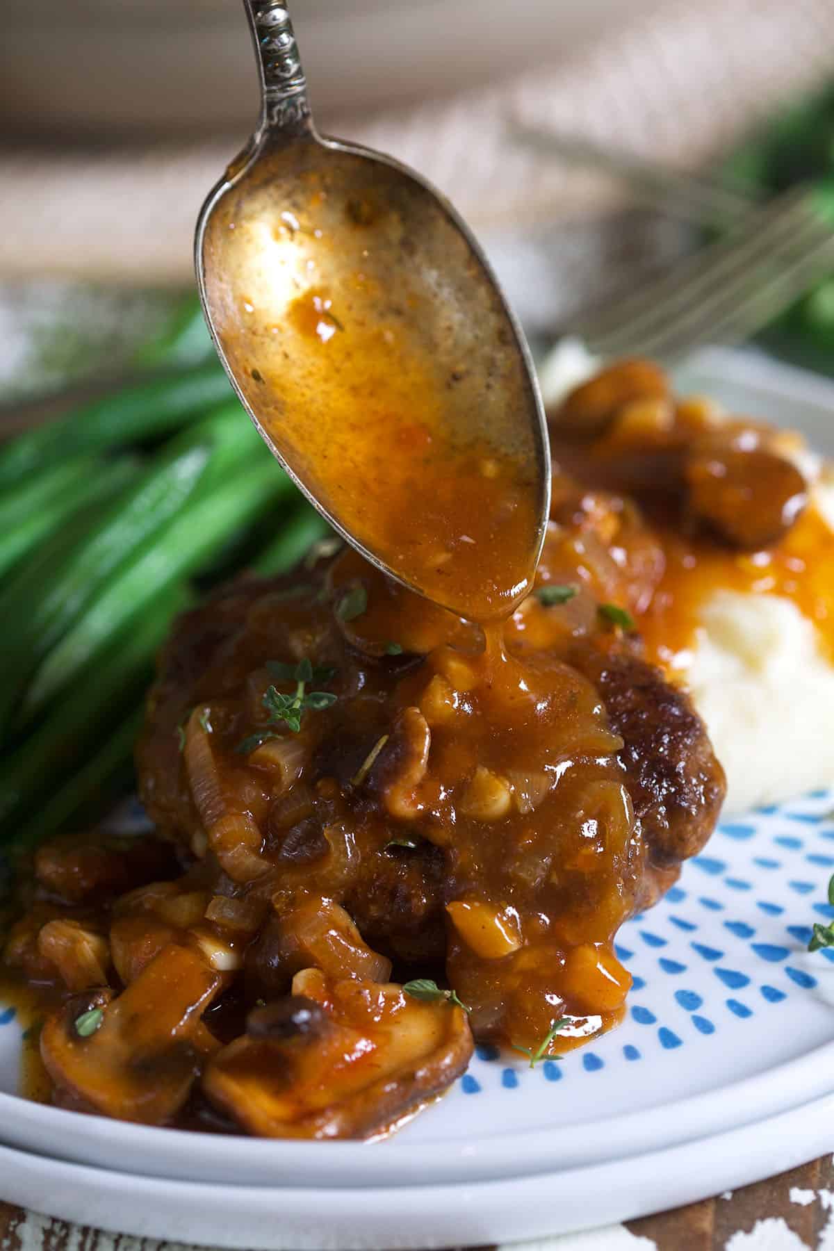 A spoon is drizzling gravy onto a steak.