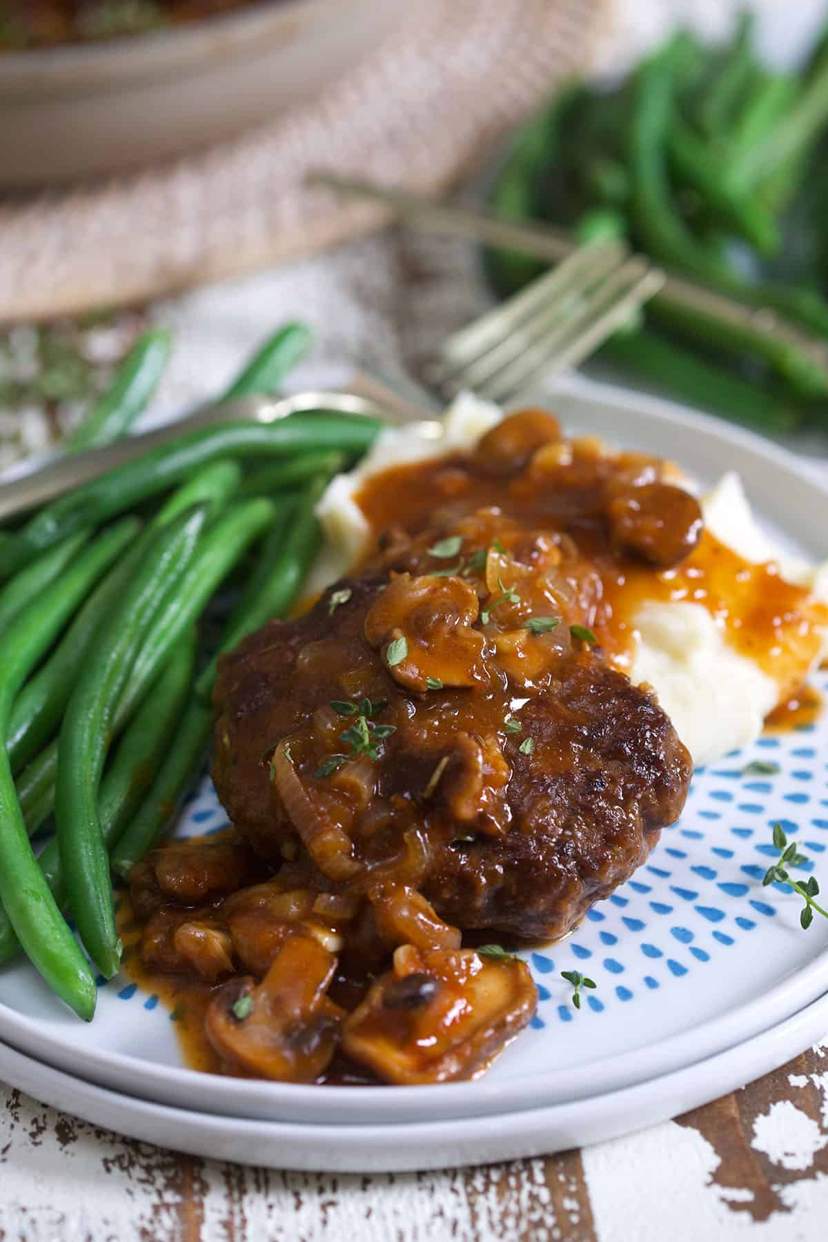 Gravy is drizzled across a hamburger steak on a blue and white plate.