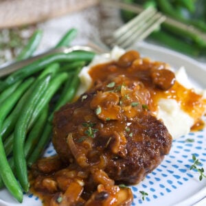 Hamburger steak is plated with green beans and mashed potatoes.