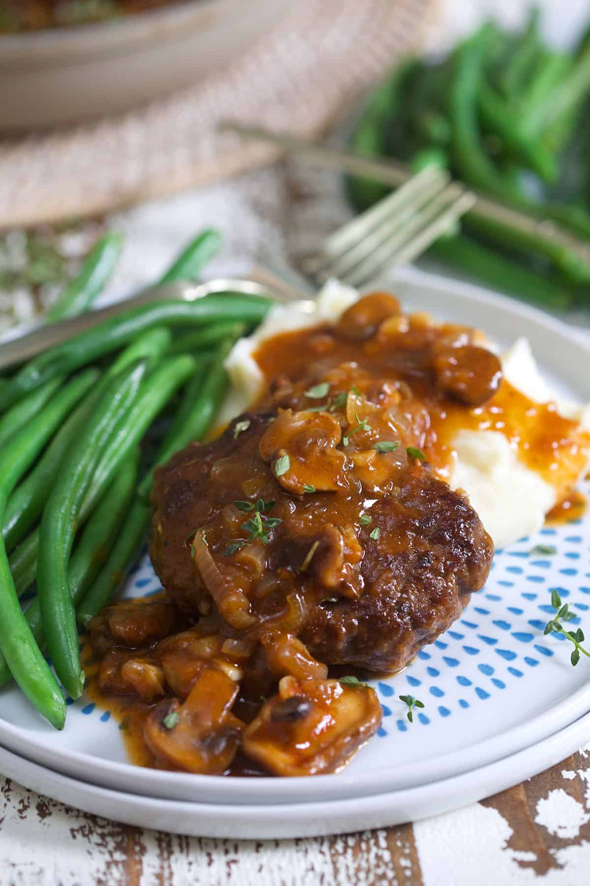 Hamburger steak is plated with green beans and mashed potatoes.