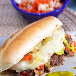 Italian Beef Sandwich on a long roll with a blue bowl of giardiniera in the background.