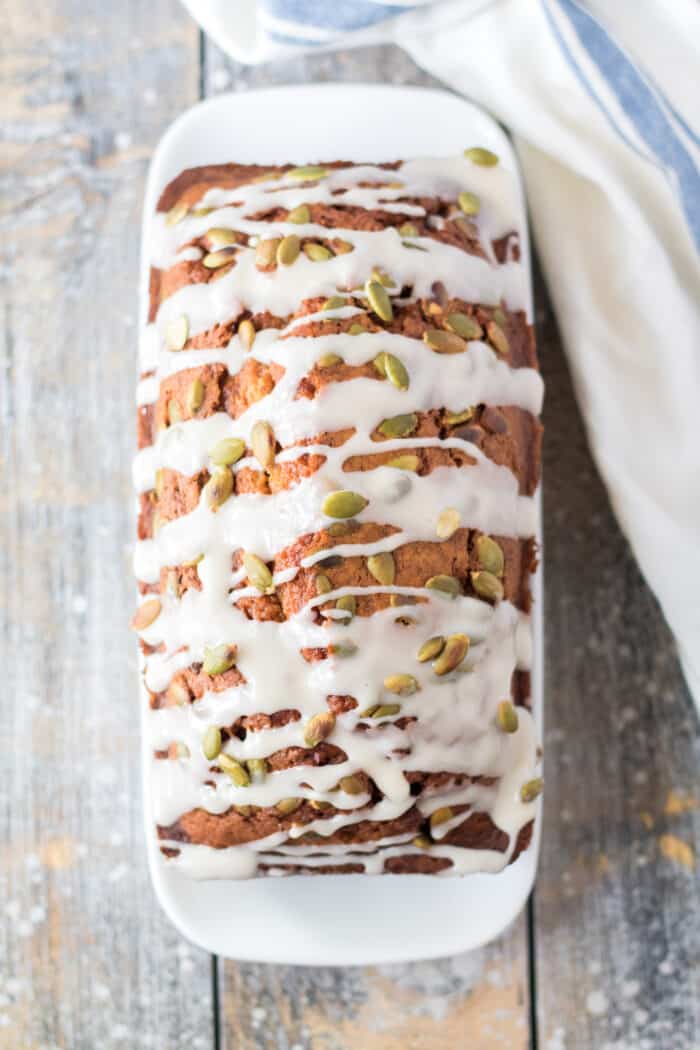 A loaf of baked and drizzled pumpkin bread is presented on a white serving plate.