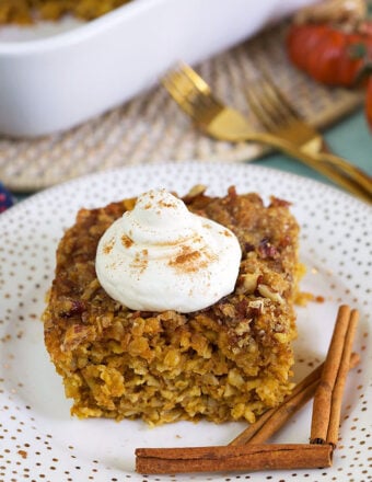 slice of baked oatmeal with whipped cream on top on a white plate with cinnamon sticks.