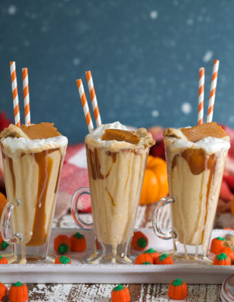 Three pumpkin pie milkshakes are in glasses, lined up on a white serving tray.