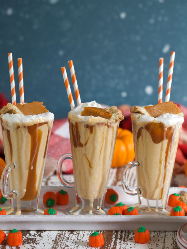 Three pumpkin pie milkshakes are in glasses, lined up on a white serving tray.
