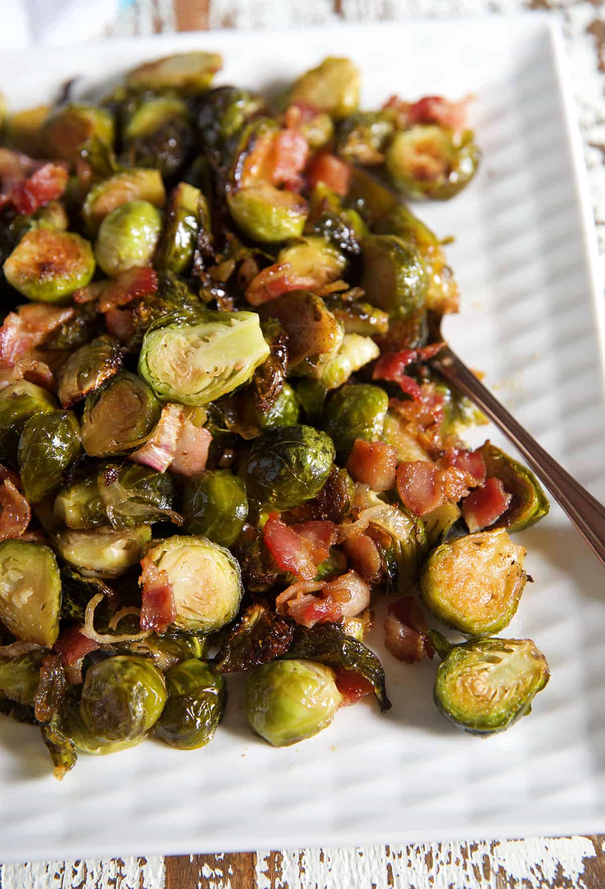 Roasted maple bacon brussel sprouts are presented on a white serving platter.