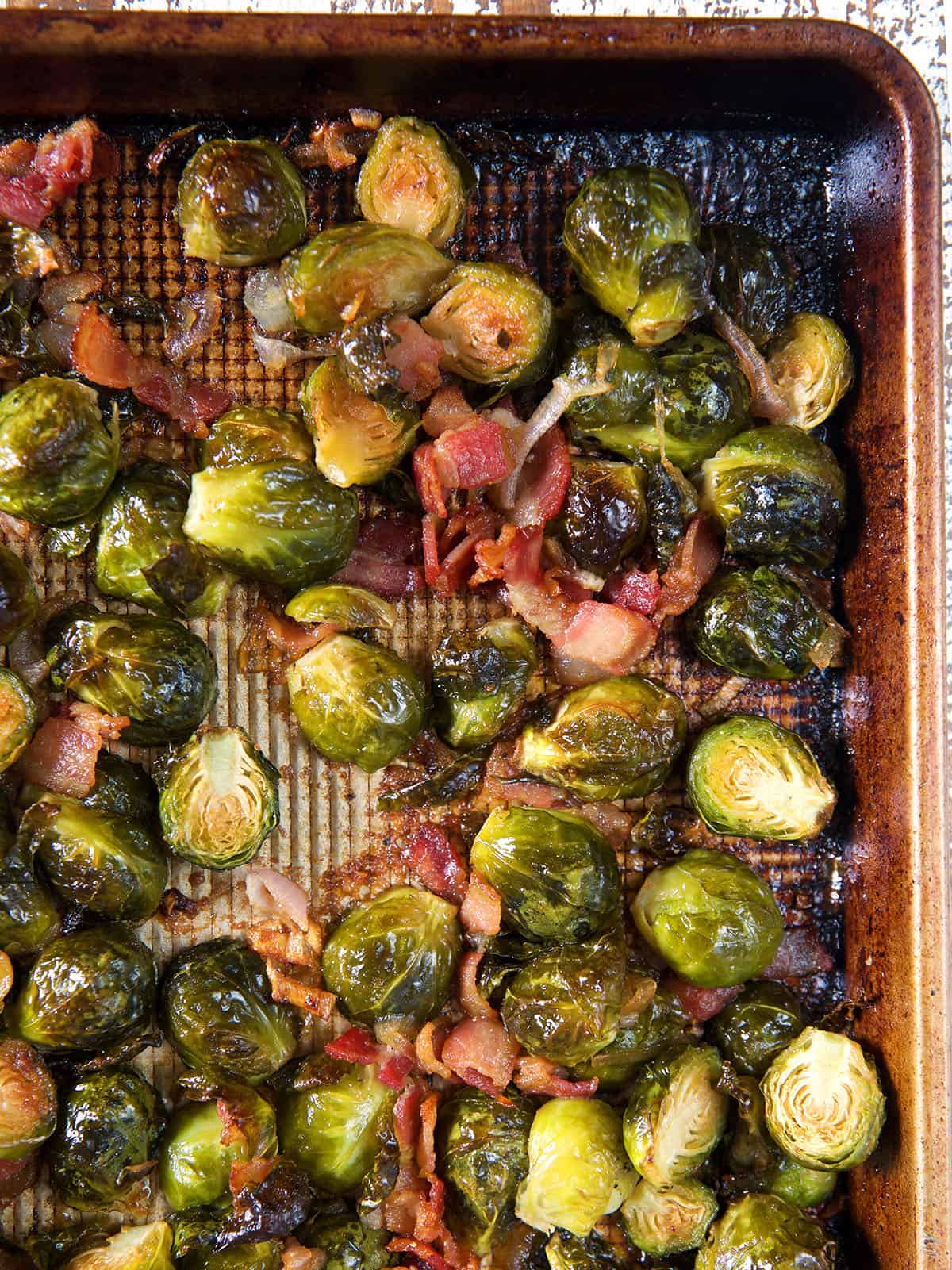 Brussel sprouts and bacon bits are spread out on a baking sheet.