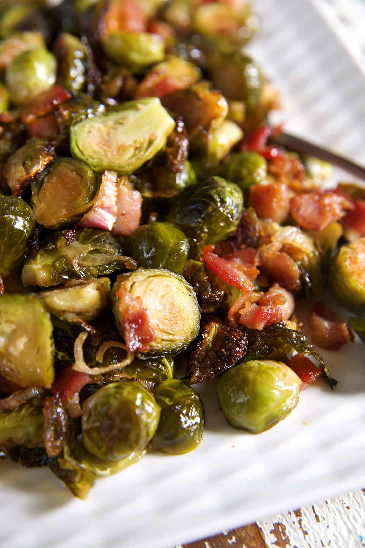 Bacon and brussel sprouts are on a white serving tray.