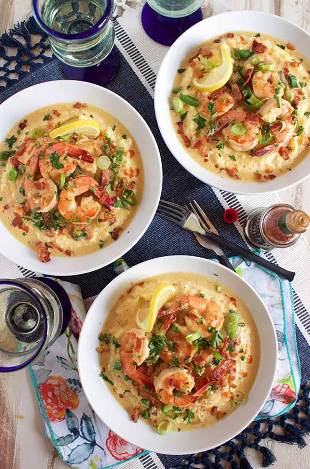 three white bowls with shrimp and grits on a blue and white table mat.