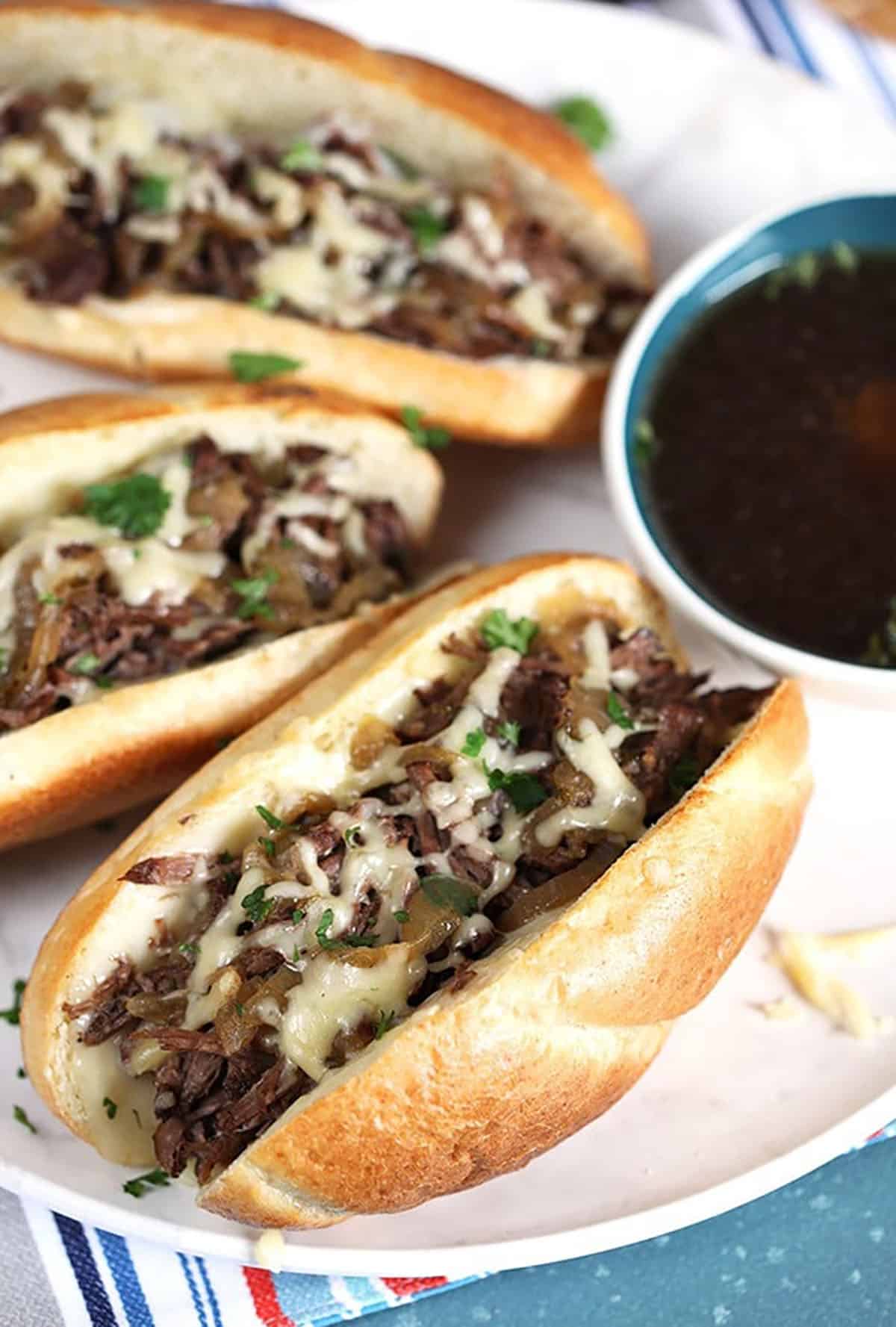 Three French dip Sandwiches on a white platter