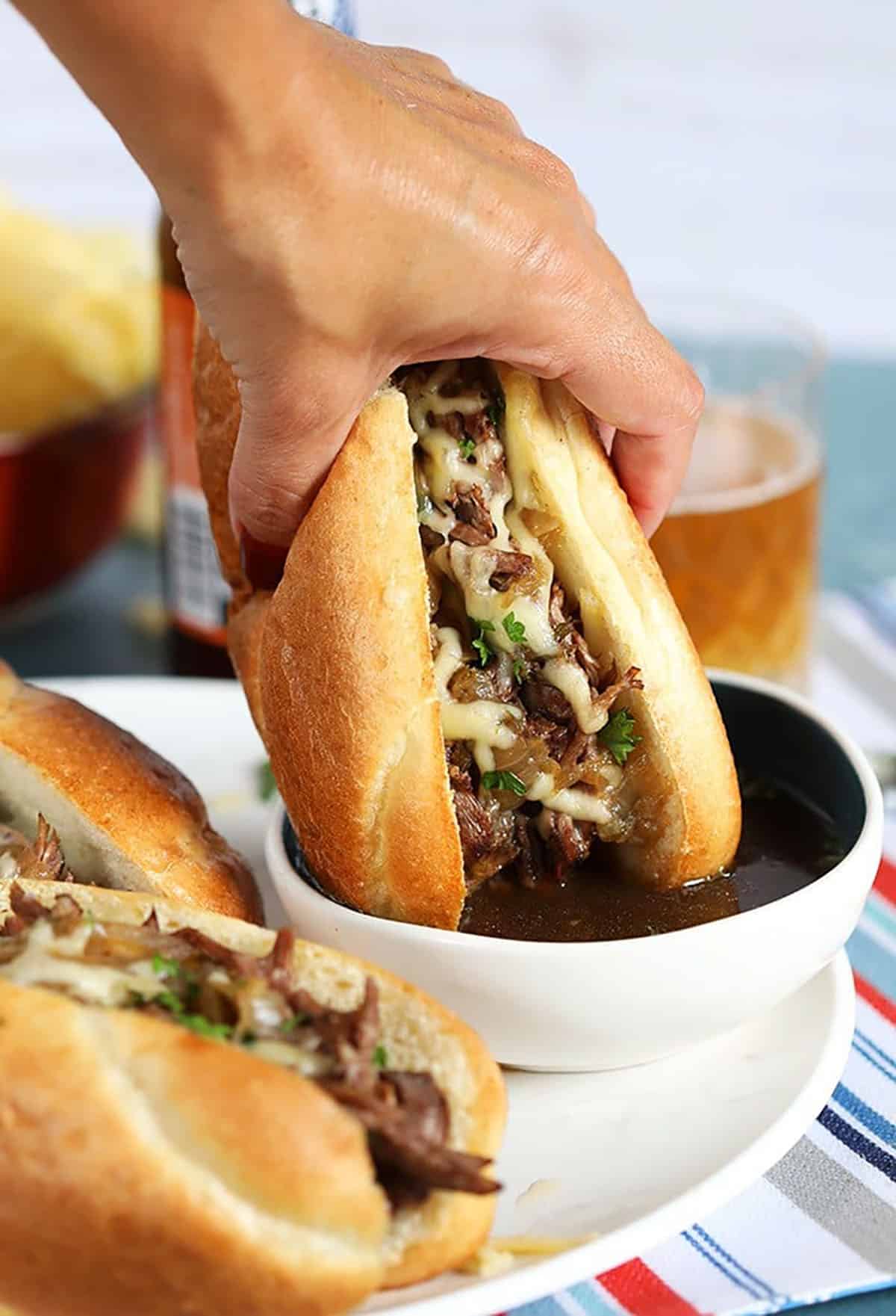 French Dip Sandwich dunked in a bowl of au jus sauce.