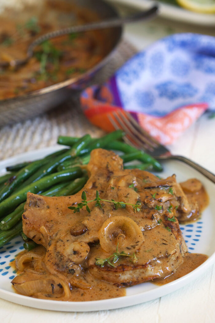 Smothered pork chops are presented next to green beans on a white plate.