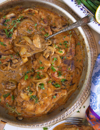 A spoon is placed in a skillet filled with gravy and pork chops.