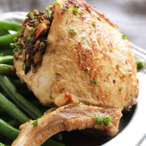 Stuffed Pork Chop with wild rice on top of a plate of green beans.