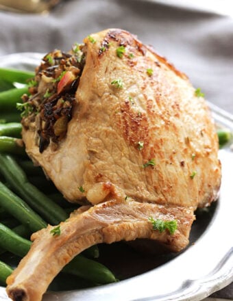 Stuffed Pork Chop with wild rice on top of a plate of green beans.