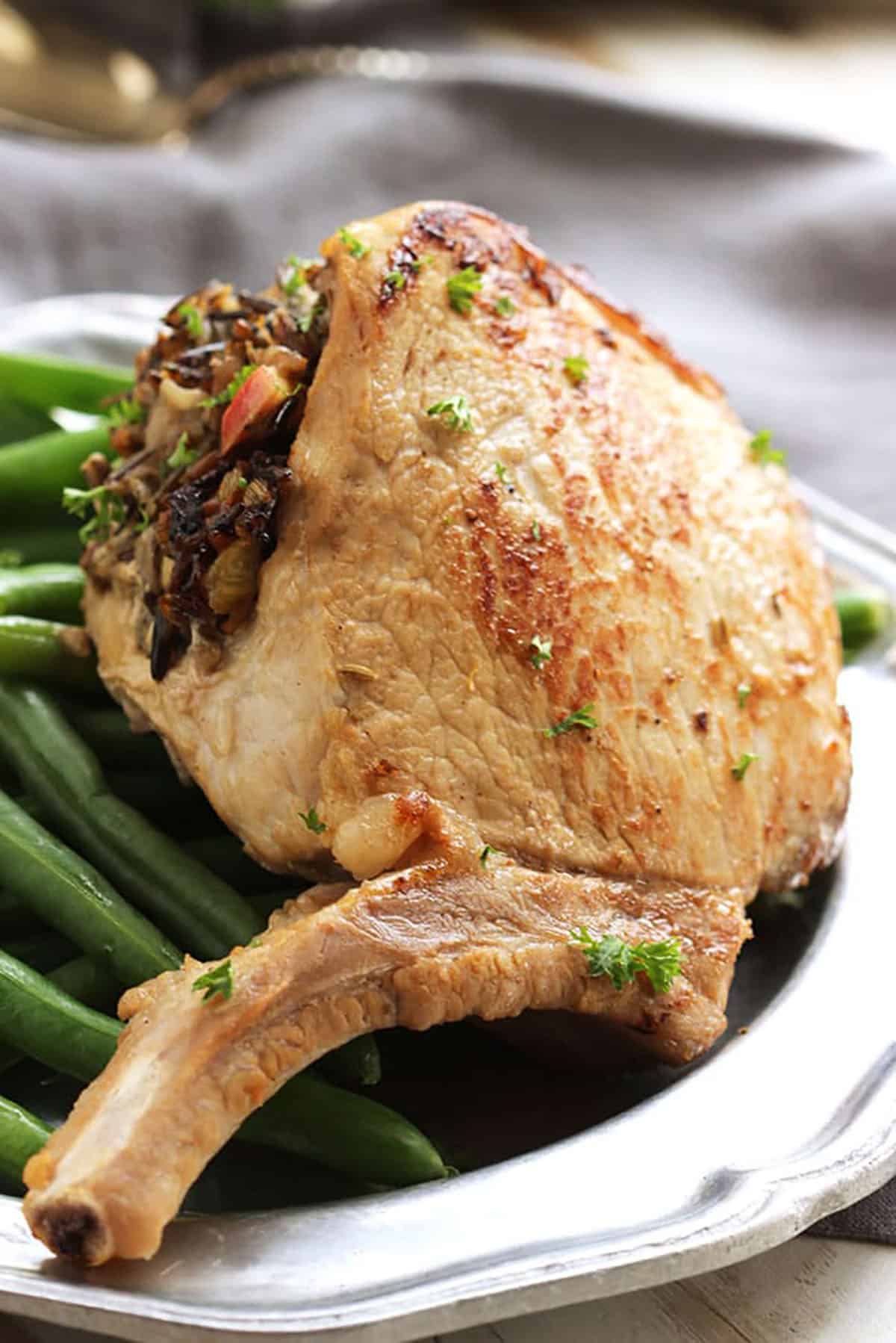 Stuffed Pork Chop with wild rice on top of a plate of green beans.