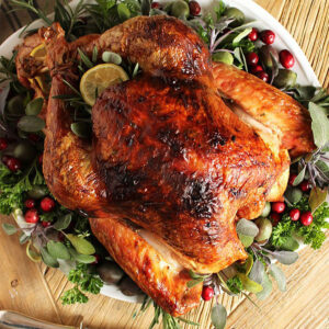 Roast Turkey for the holiday on a white platter with herbs and cranberries.