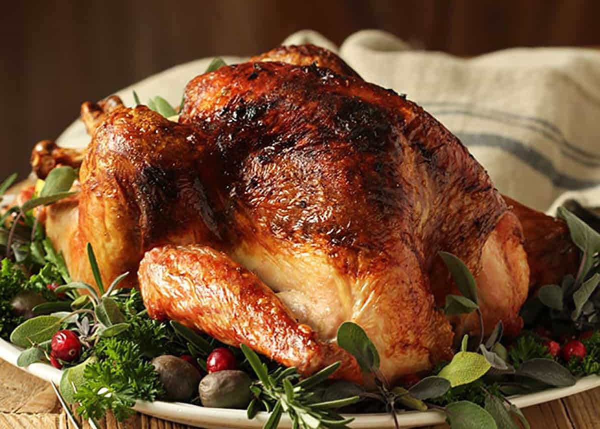 Roast turkey on a white platter garnished with herbs and a rustic linen in the background.