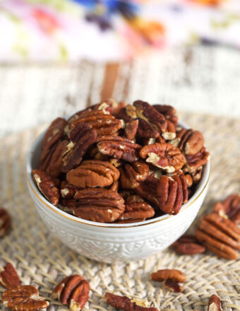 A small white bowl is filled with toasted pecans.