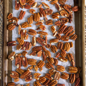 Pecans are spread out on a lined baking sheet.