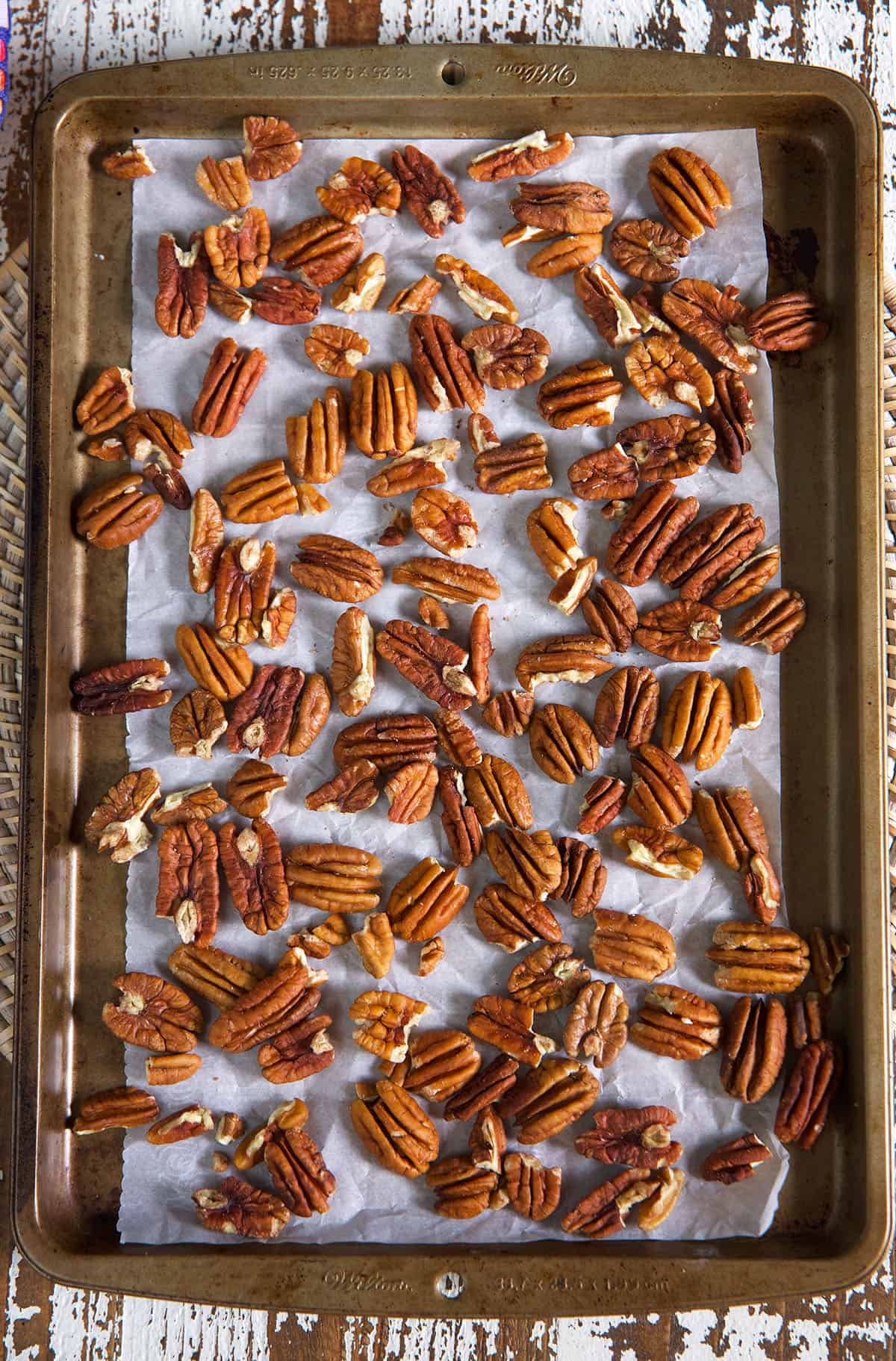 Pecans are spread out on a lined baking sheet.