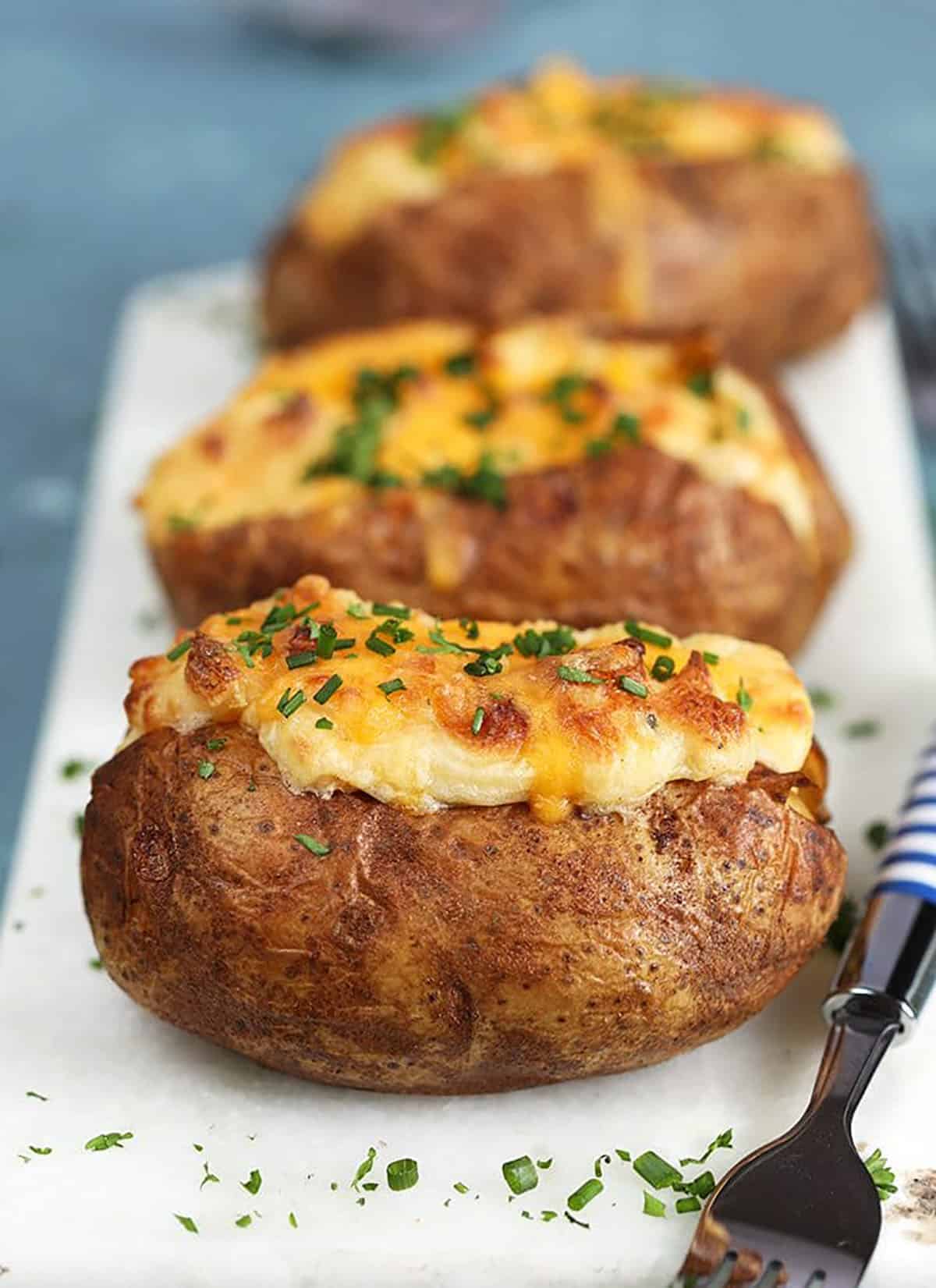 Twice Baked Potatoes with Cheddar and Chives on a white marble board.