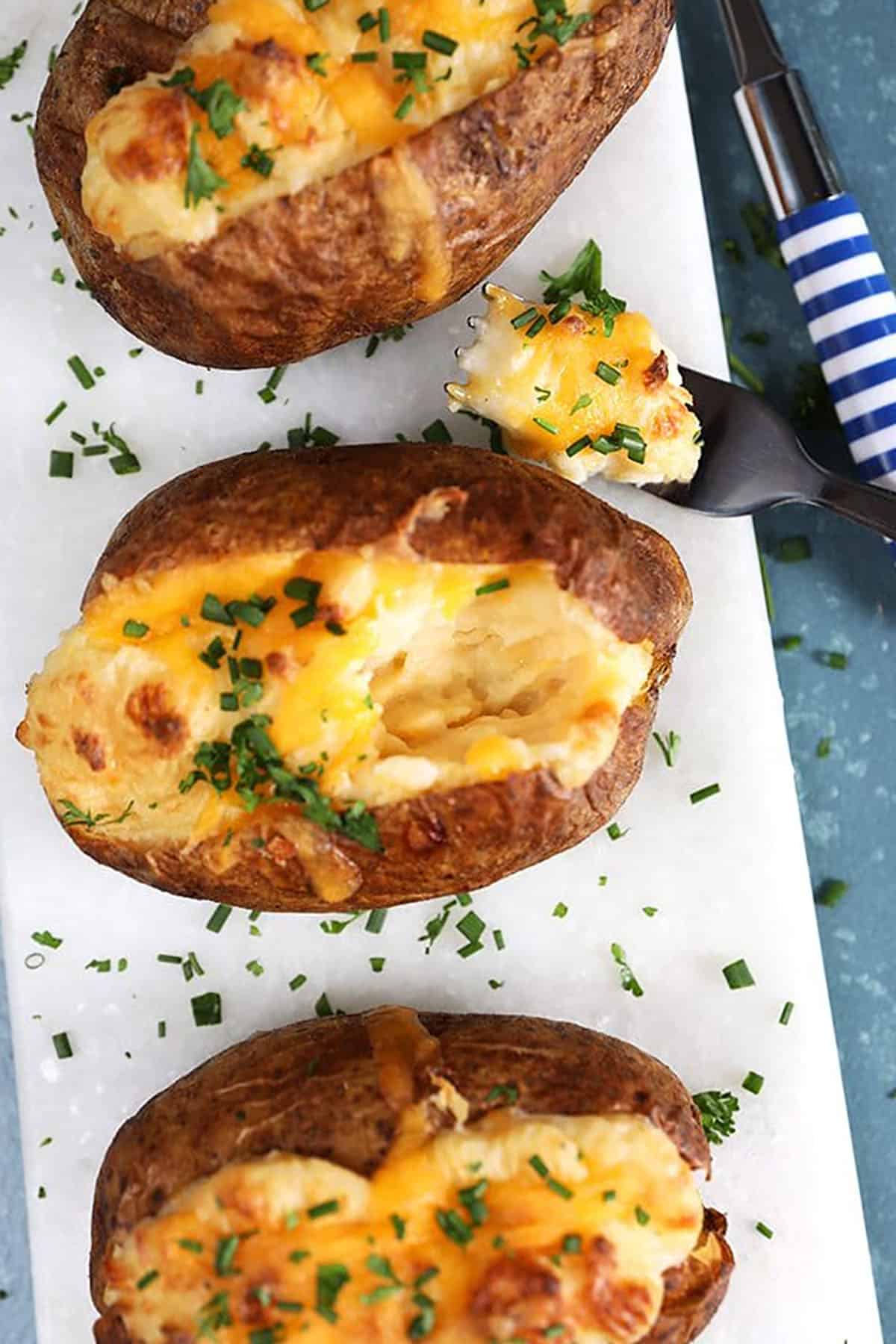 Overhead shot of twice baked potatoes on a white board with a blue and white striped fork.