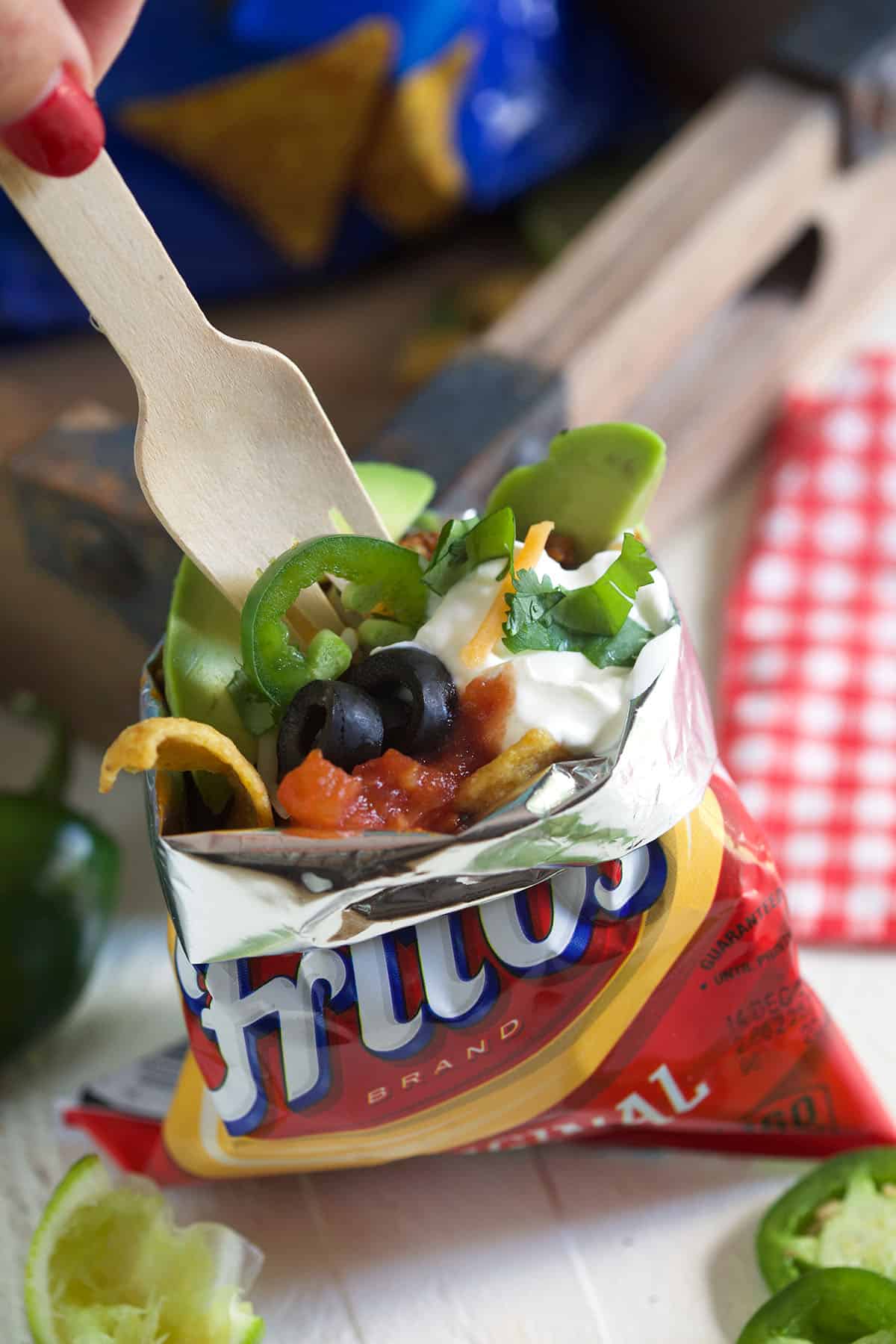 A fork is digging into a bag of frito's that's filled with all sorts of taco ingredinets. 