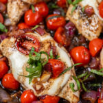A close up photo shows cooked tomatoes, onion, chicken, and basil.