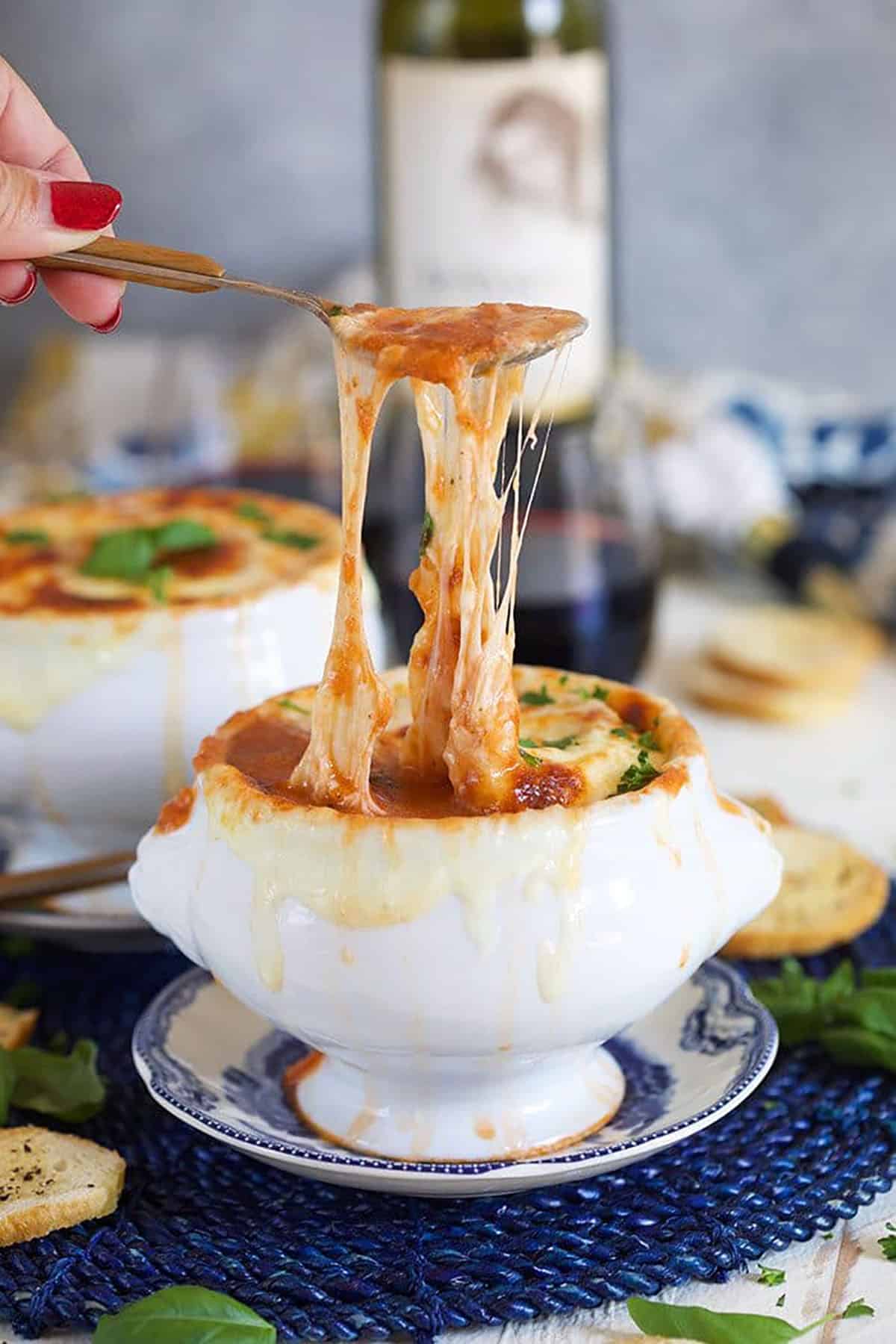 Super cheesy Baked Tomato Bisque with a spoon pulling melty cheese.