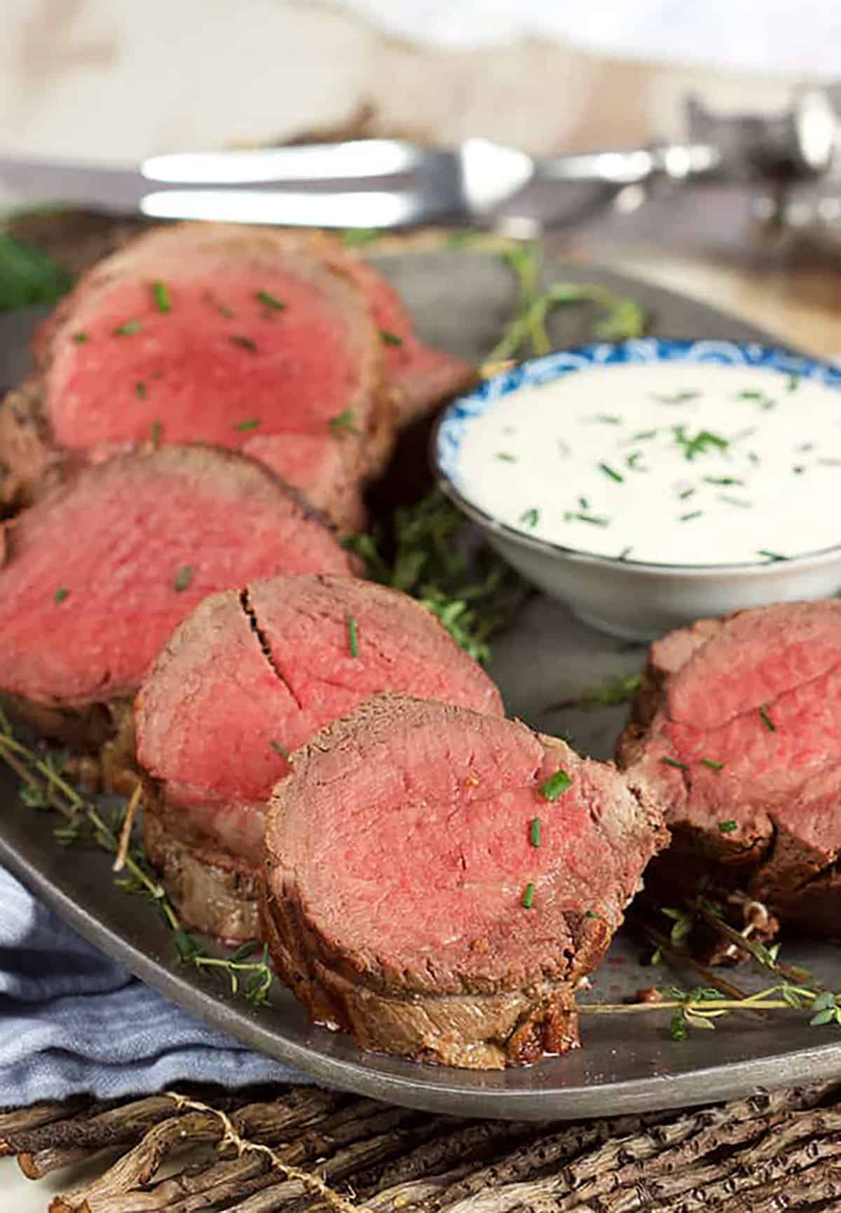 Beef Tenderloin sliced on a pewter platter with a bowl of horseradish sauce.