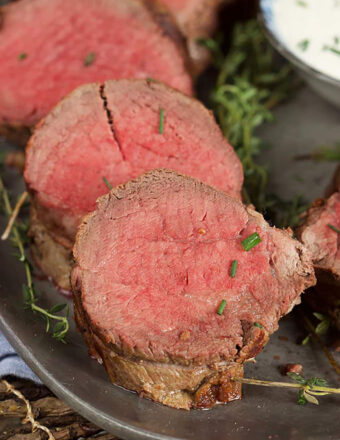 three slices of beef tenderloin on a platter sprinkled with chopped chives