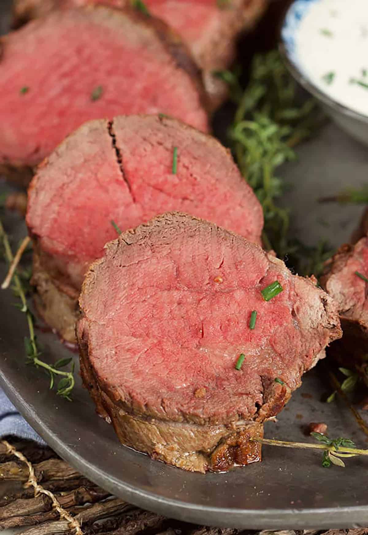 three slices of beef tenderloin on a platter sprinkled with chopped chives