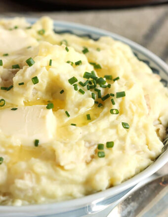 Mashed Potatoes in a blue and white bowl topped with chives and a pat of butter.