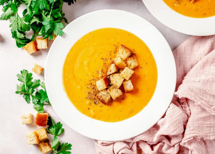 Croutons are placed on top of and next to a bowl of soup.