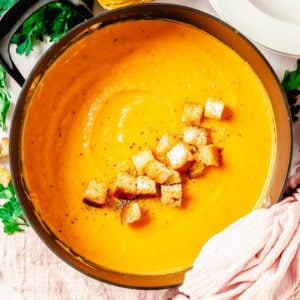 Butternut squash soup is presented in a large black pot and topped with croutons.